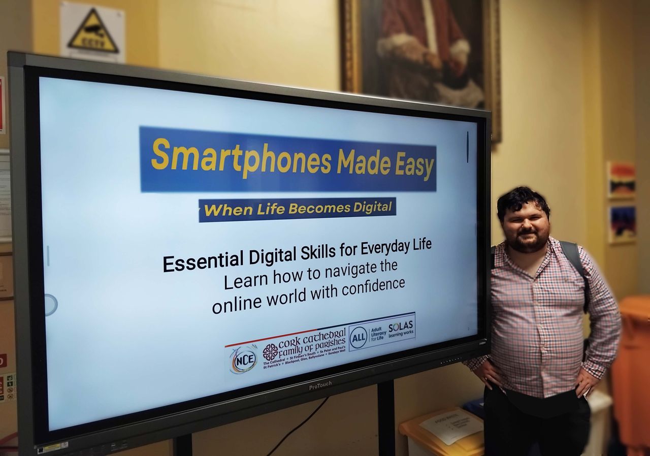 A man stands next to a large screen displaying a presentation titled 